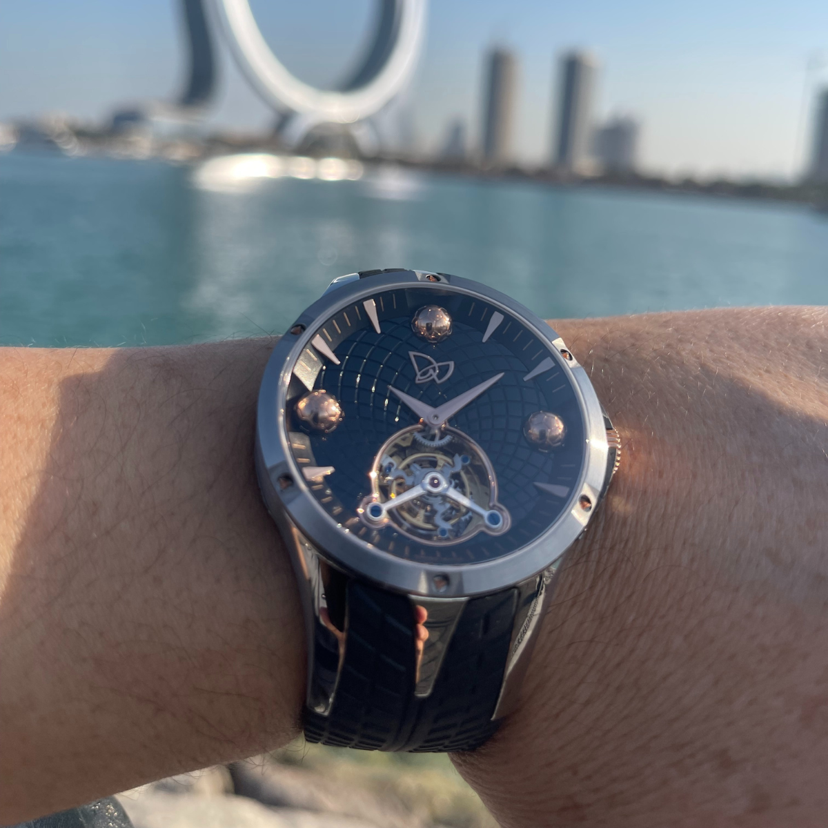 Watch on a wrist with a scenic background of water and structures.