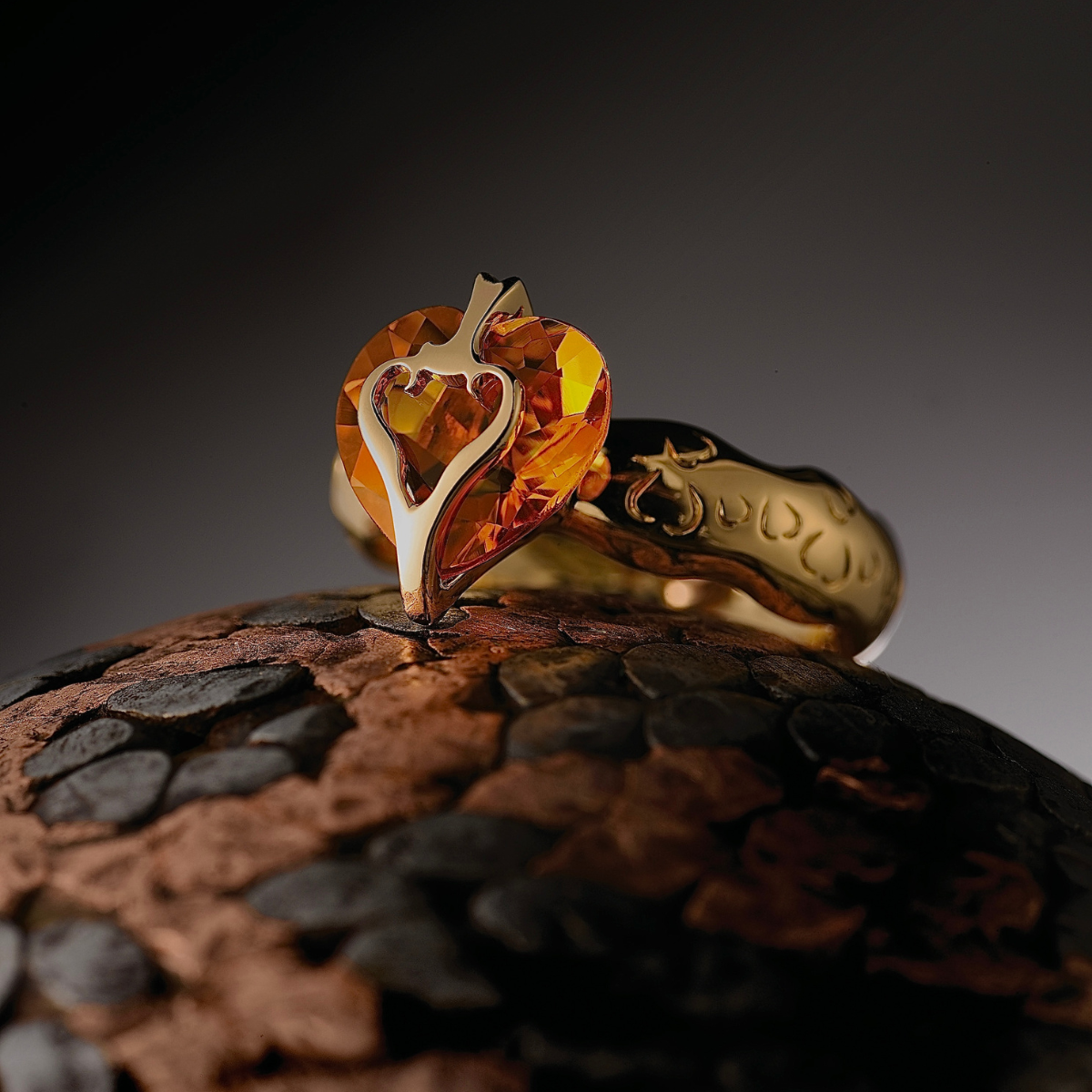 Gold ring with a heart-shaped amber stone on a dark background