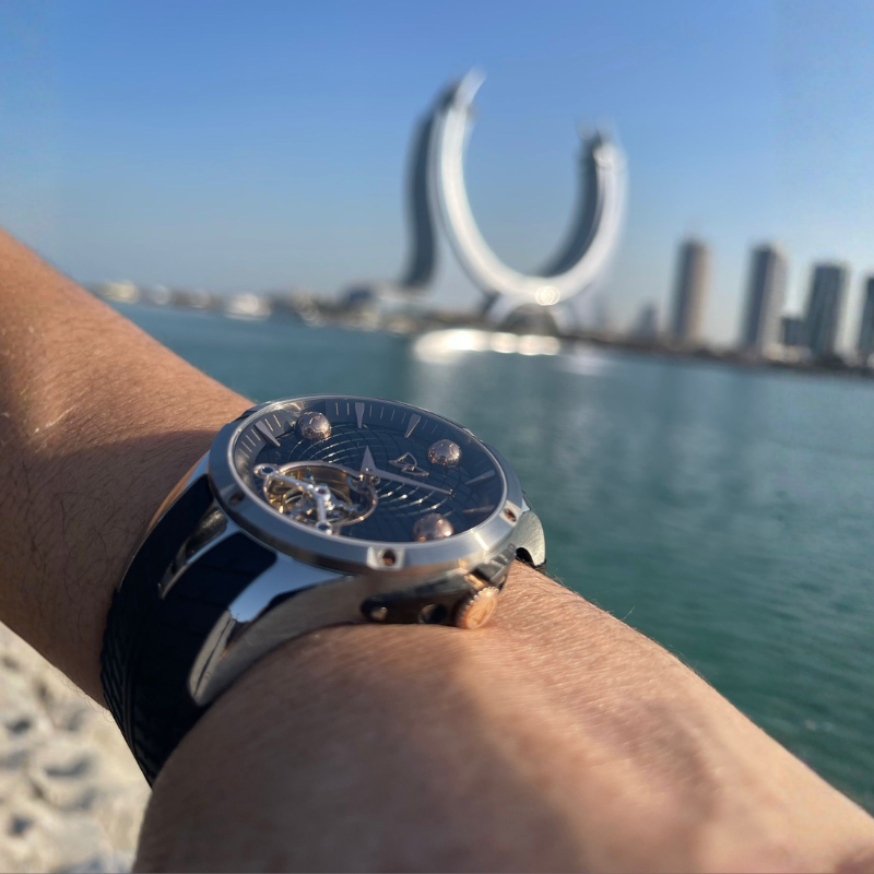 Silver watch on a wrist with a cityscape and water in the background